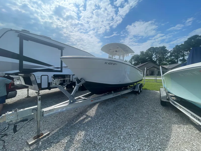 The Image of 2020 Cobia 262 Center Console boat on trailer, parked beside RV under cloudy sky. - 0