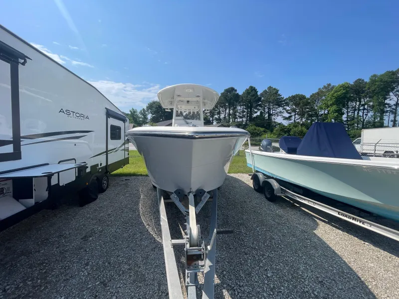 The Image of 2020 Cobia 262 Center Console boat on trailer, parked between RV and another boat. - 1