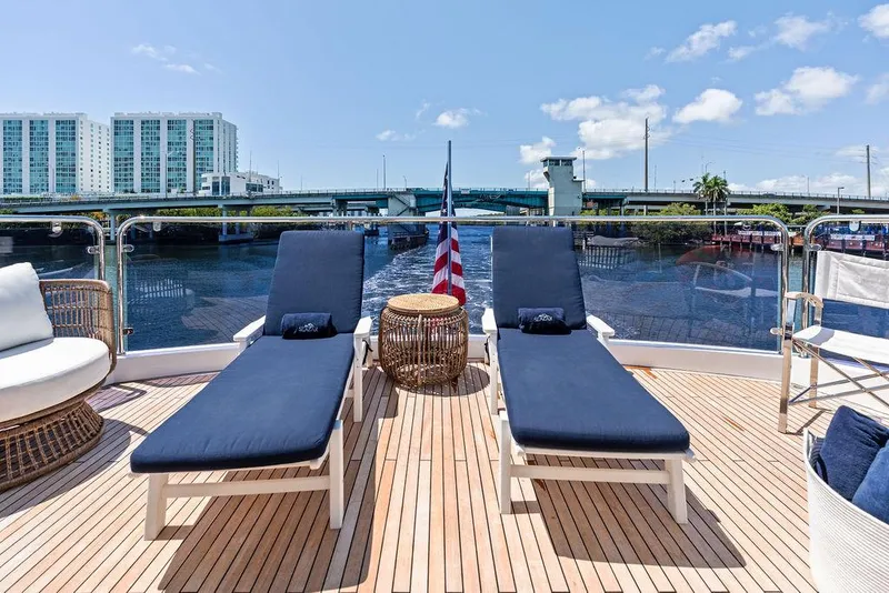 Slide: The Image of Sunseeker 86 Yacht 2019 deck with lounge chairs, American flag, and waterfront view. - 29