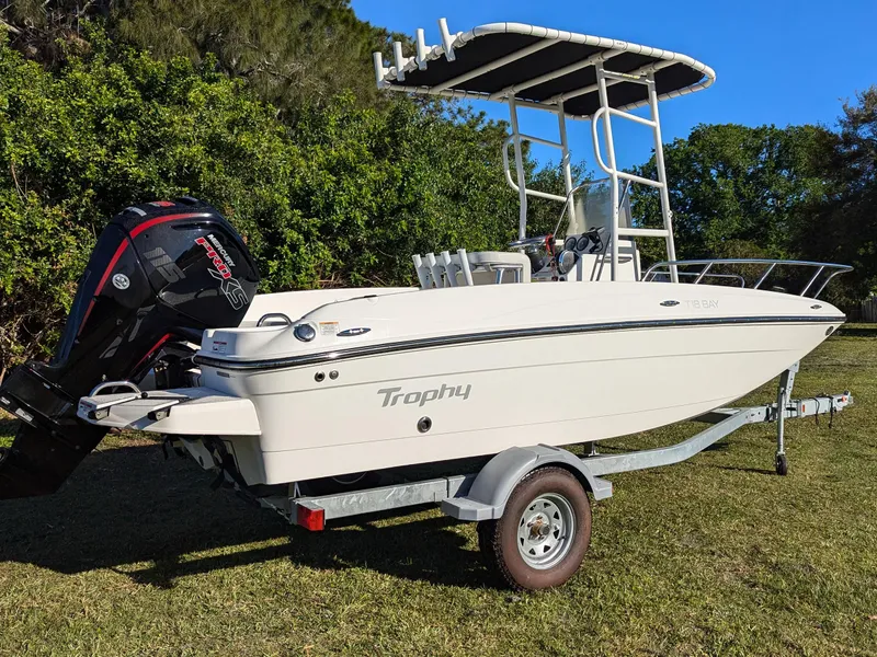 Slide: The Image of 2024 Bayliner Trophy T18 boat on trailer, parked on grass with trees in background. - 2