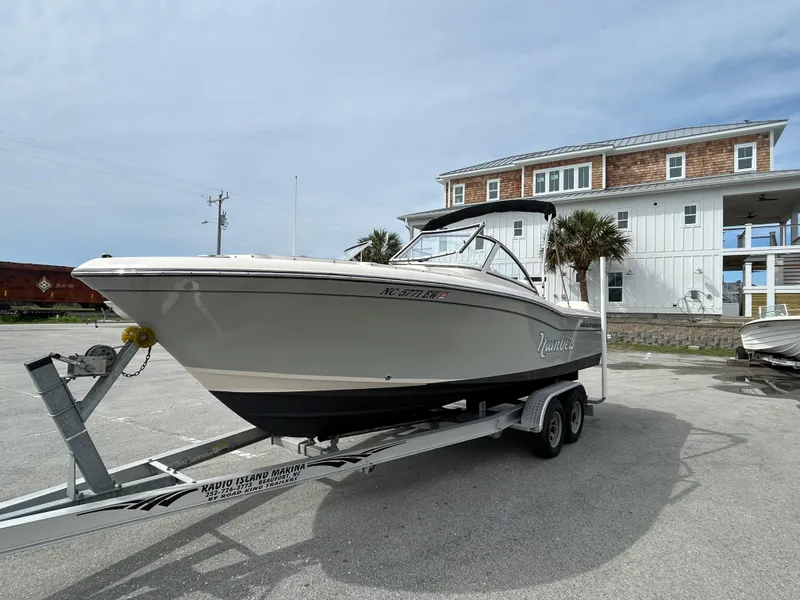 Slide: The Image of 2022 Grady-White Freedom 215 boat on trailer, parked near a coastal house. - 2
