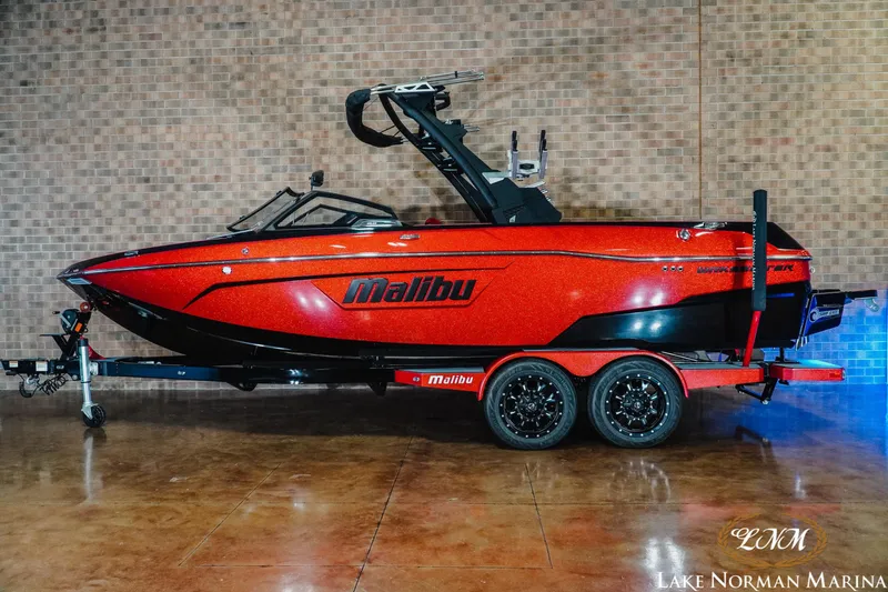 Slide: The Image of 2021 Malibu 23 LSV boat in vibrant red on a trailer, displayed indoors. - 1