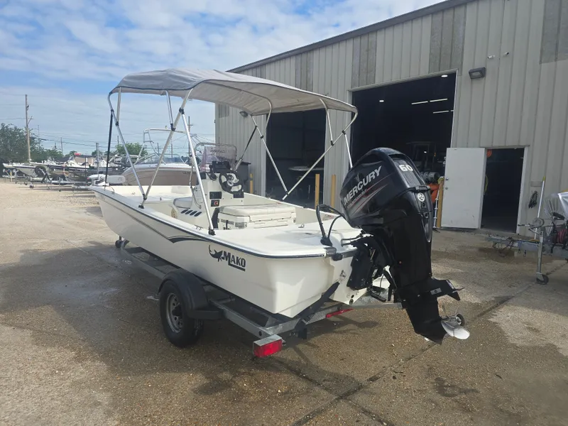 Slide: The Image of 2019 Mako Pro Skiff 17 CC boat with Mercury engine, parked outside a warehouse. - 2