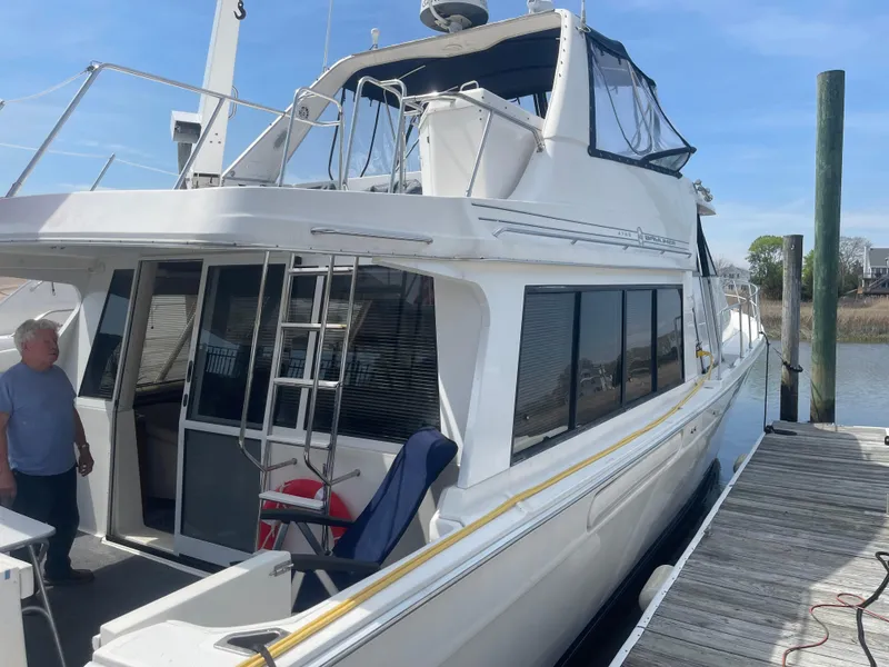 Slide: The Image of 1999 Bayliner 4788 Motoryacht docked, featuring spacious deck and upper helm station. - 2