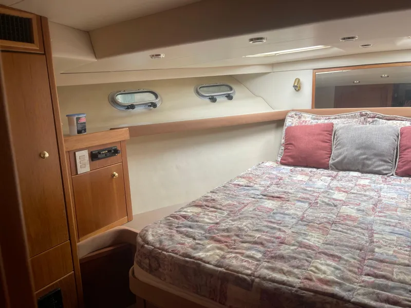Slide: The Image of 1999 Bayliner 4788 Motoryacht bedroom with cozy bed, wooden cabinetry, and porthole windows. - 27