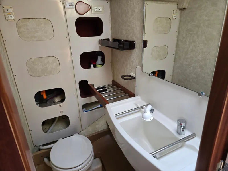 Slide: The Image of Compact bathroom in a 1985 Amel Maramu sailboat, featuring a sink, toilet, and storage shelves. - 34