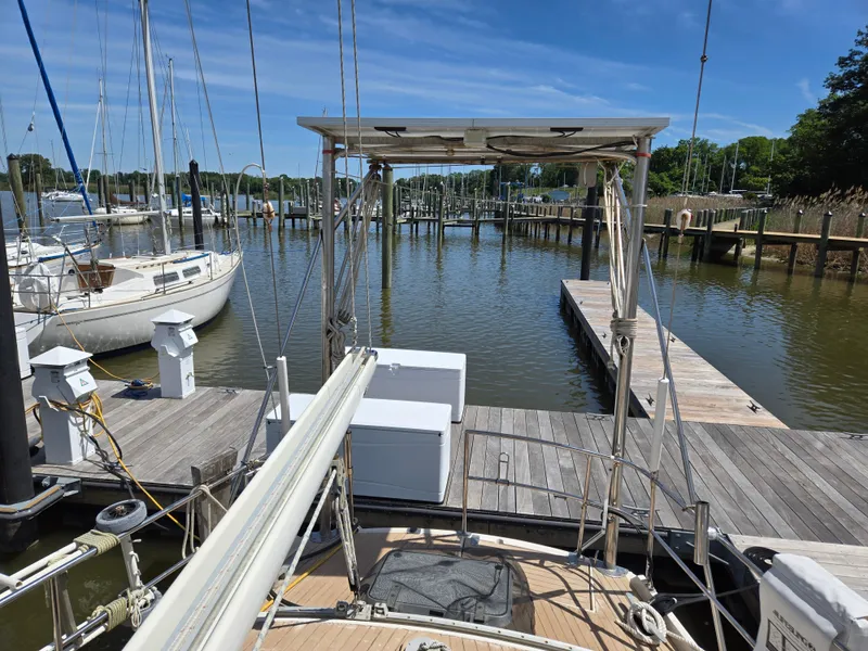 Slide: The Image of 1985 Amel Maramu sailboat docked at a marina, surrounded by calm water and other boats. - 47
