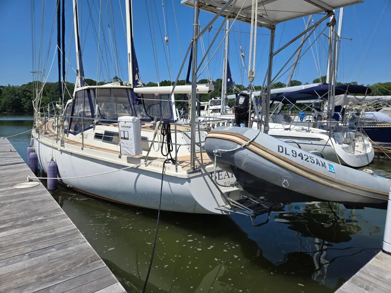 Slide: The Image of 1985 Amel Maramu sailboat docked with dinghy, clear sky, calm water. - 49