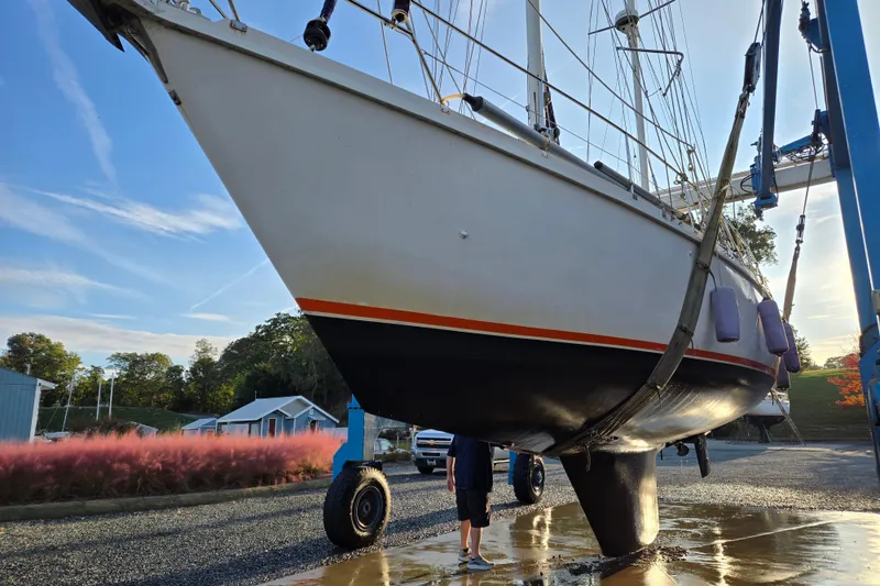 Slide: The Image of 1985 Amel Maramu sailboat on dry dock, with blue sky and greenery in background. - 51