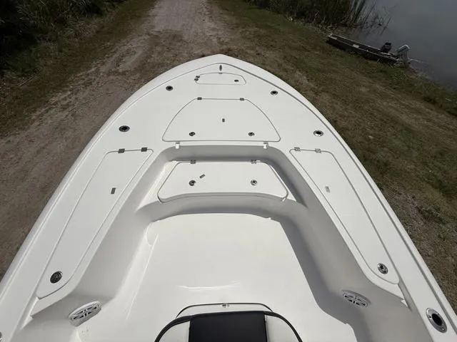Slide: The Image of 2024 Tidewater 2410 Bay Max boat, white deck, storage compartments, parked on a dirt path near water. - 17