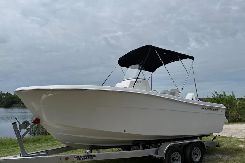 The Image of 2024 Aquasport 2100 CC boat on trailer by a lake under cloudy sky. - 0