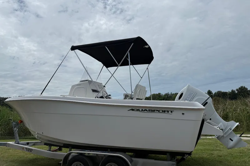 Slide: The Image of 2024 Aquasport 2100 CC boat on trailer, featuring sleek design and canopy. - 2