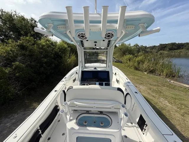 Slide: The Image of 2024 Tidewater 256 CC Adventure boat with advanced console and rod holders, docked near lush greenery. - 16