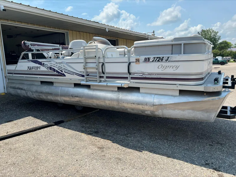 Slide: The Image of 2003 Manitou Osprey pontoon boat parked outside a garage on a sunny day. - 0