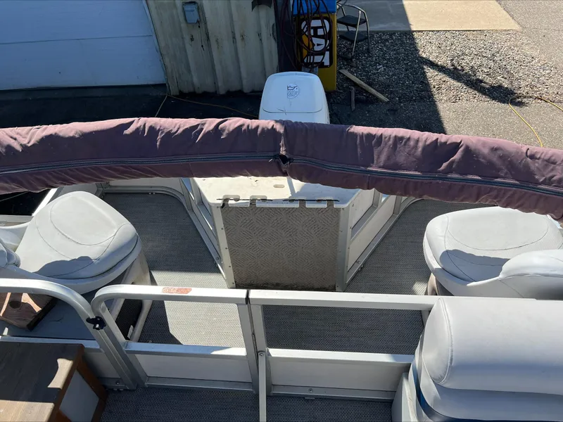 Slide: The Image of 2003 Manitou Osprey boat interior with seating and covered railing, parked outdoors. - 5