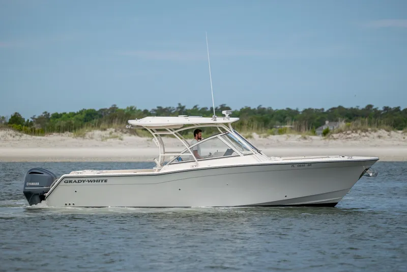 Slide: The Image of 2020 Grady-White Freedom 307 boat cruising on calm water near a sandy shoreline. - 0