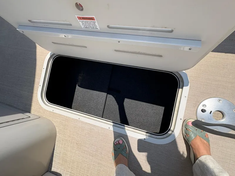 Slide: The Image of Open storage compartment on 2020 G3 SunCatcher boat, with beige carpet and visible feet. - 24