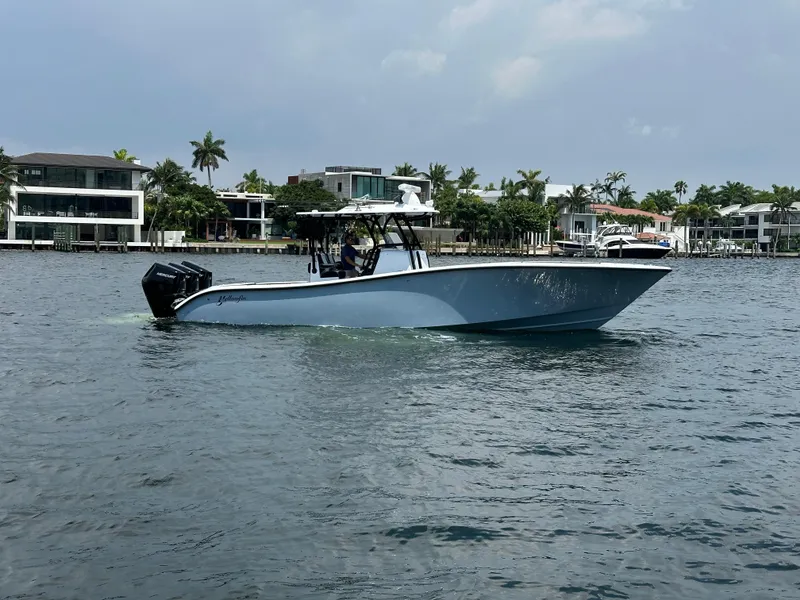 Slide: The Image of 2024 Yellowfin 34 Offshore boat cruising on a calm waterfront with modern homes in the background. - 0
