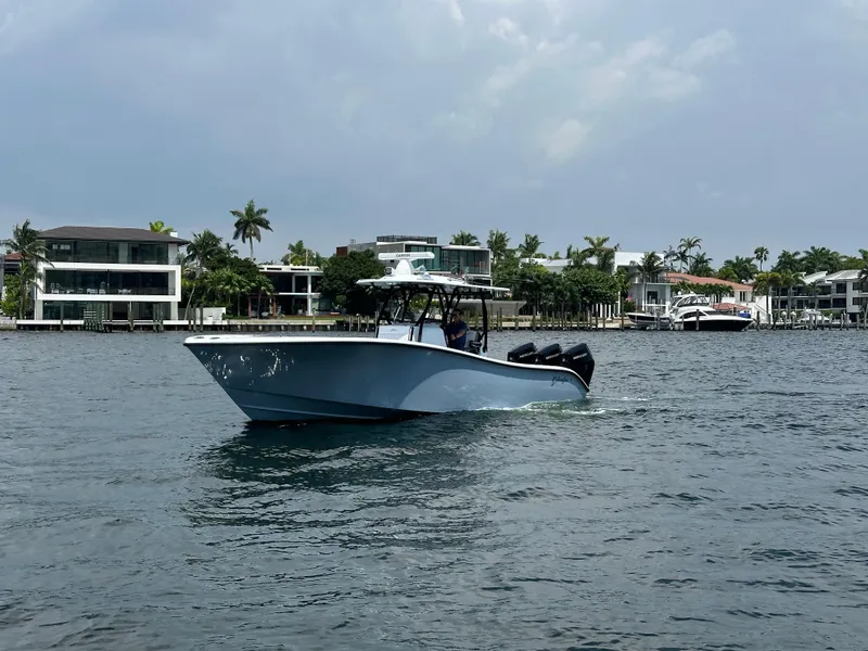 Slide: The Image of 2024 Yellowfin 34 Offshore boat cruising near waterfront homes under a cloudy sky. - 3