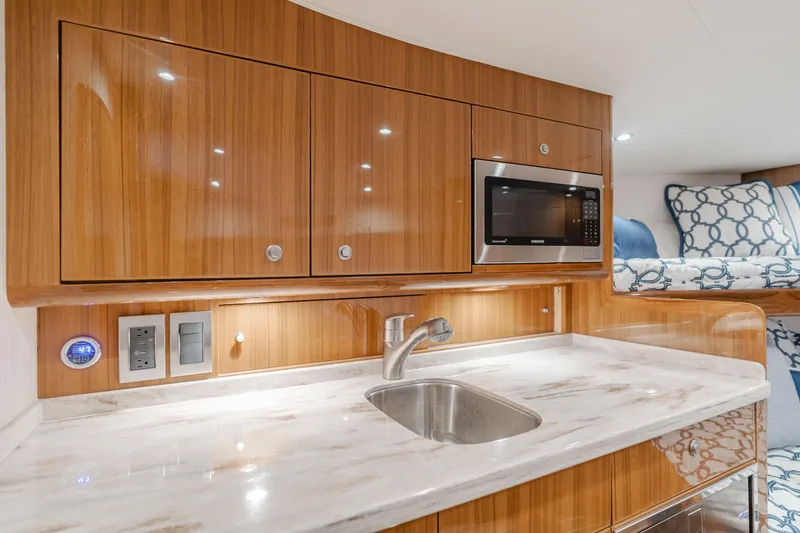 Slide: The Image of 2022 Viking 38 Open Billfish interior with kitchenette, featuring wood cabinets and a microwave. - 5