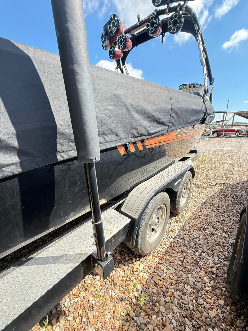 Slide: The Image of 2012 Epic 23V boat on trailer, covered, with speakers, parked on gravel. - 9