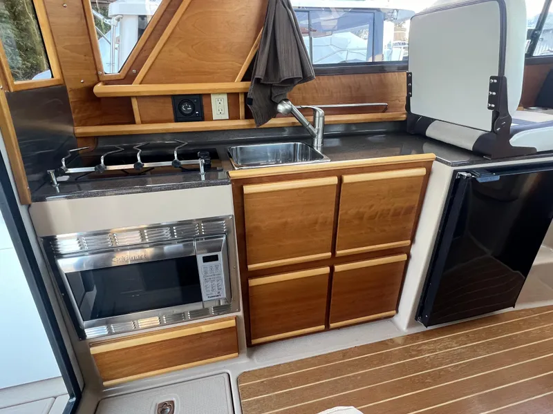 Slide: The Image of 2016 Cutwater C28 boat kitchen with stove, sink, microwave, and wooden cabinetry. - 33