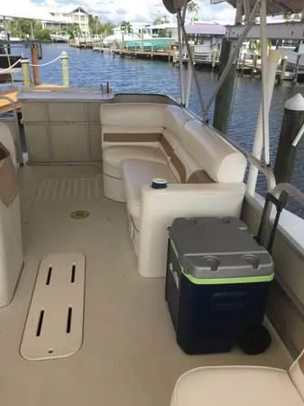 Slide: The Image of 1997 Sylvan Deck Boat interior with seating and cooler, docked by a waterfront. - 10