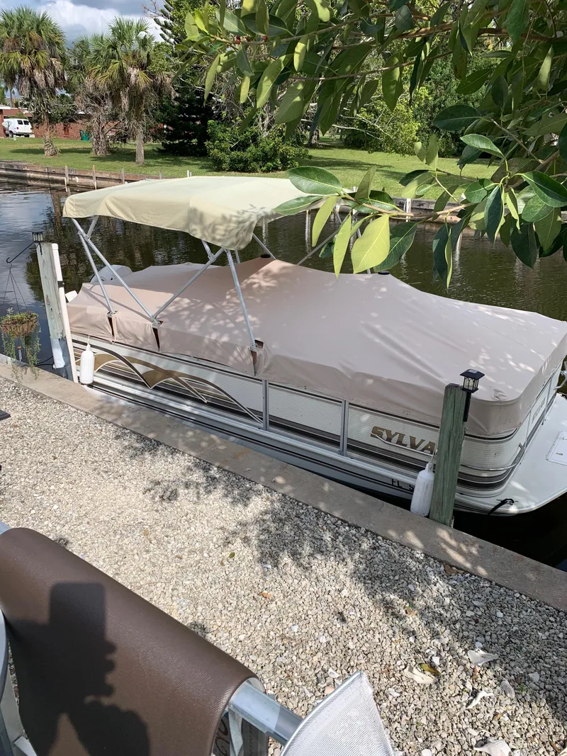 Slide: The Image of 1997 Sylvan Deck Boat docked by a leafy canal, covered and shaded. - 2