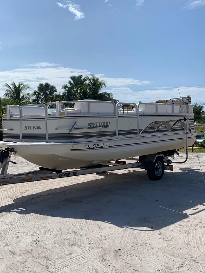 Slide: The Image of 1997 Sylvan Deck Boat on trailer, parked outdoors under clear sky. - 3