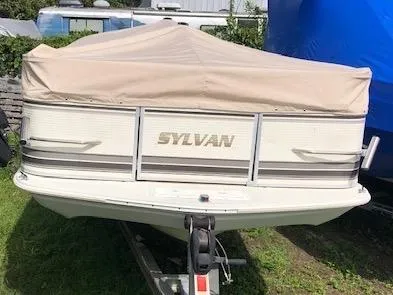 Slide: The Image of 1997 Sylvan Deck Boat with beige cover on trailer, parked on grass. - 5