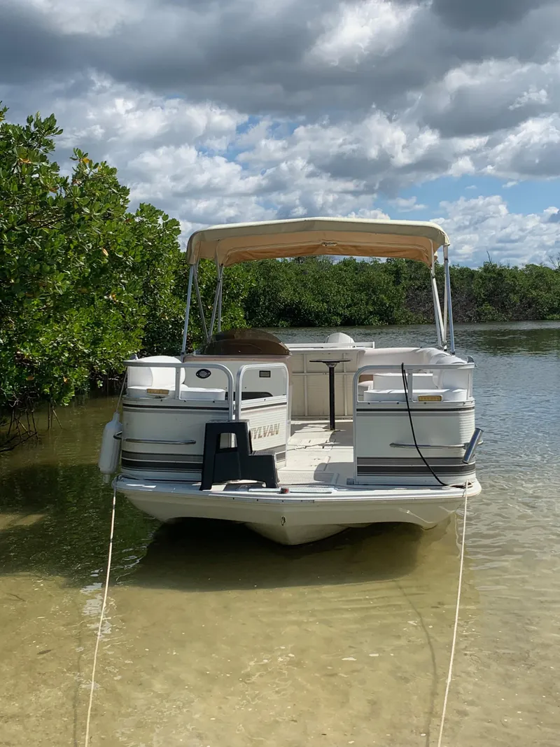 Slide: The Image of 1997 Sylvan Deck Boat moored in shallow water under a cloudy sky. - 6