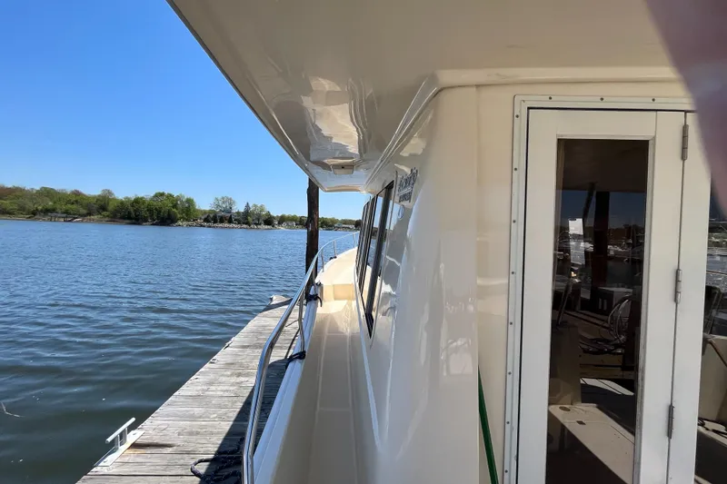 Slide: The Image of 2005 Mainship 400 Trawler docked by a serene lake under clear blue skies. - 14