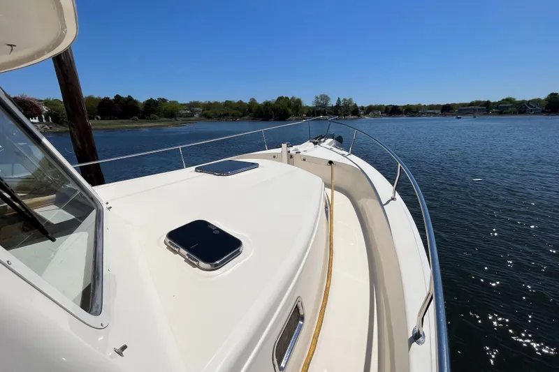 Slide: The Image of 2005 Mainship 400 Trawler on calm water, showcasing deck and railing under clear blue sky. - 19
