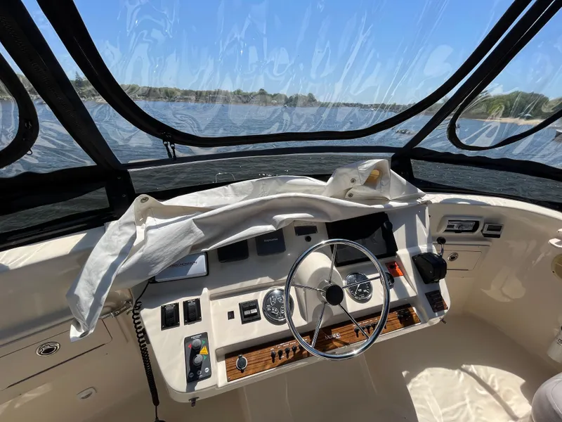 Slide: The Image of 2005 Mainship 400 Trawler helm with steering wheel, gauges, and controls, overlooking water. - 34