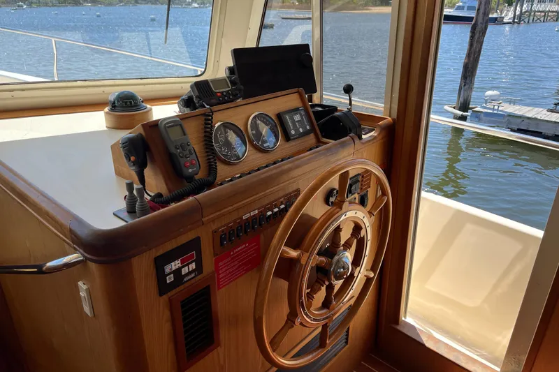 Slide: The Image of 2005 Mainship 400 Trawler helm with wooden wheel, gauges, and navigation equipment by the water. - 43