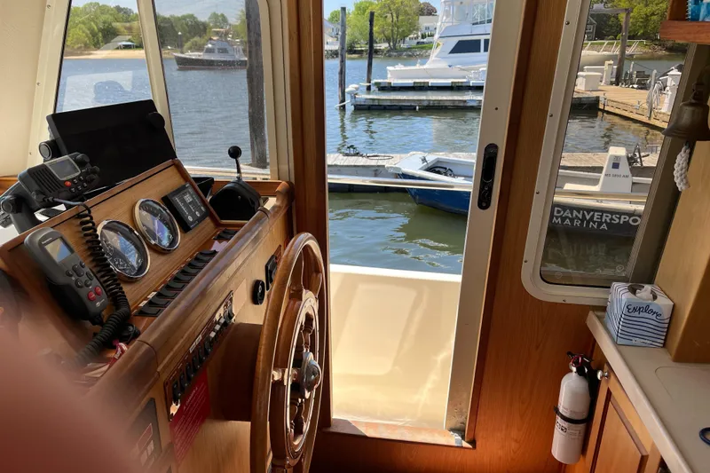 Slide: The Image of 2005 Mainship 400 Trawler helm with marina view, featuring classic wooden steering wheel. - 49