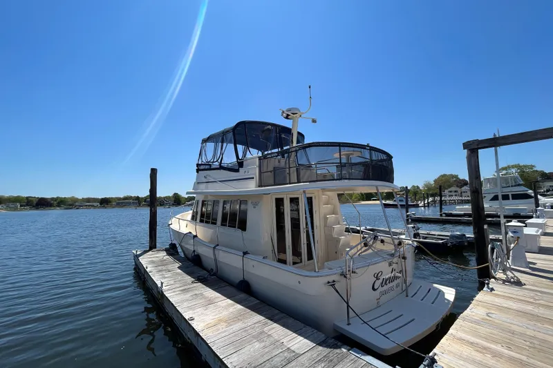 Slide: The Image of 2005 Mainship 400 Trawler docked on a sunny day, featuring upper deck and calm waters. - 7