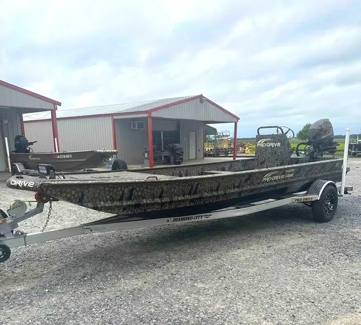 Slide: The Image of 2025 Pro-Drive 2054 X Series TD boat on trailer, parked near metal buildings. - 6