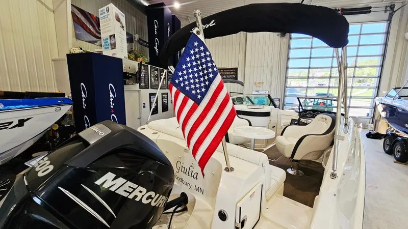 Slide: The Image of 2014 Sea Ray 220 Sundeck Outboard with American flag in showroom. - 25