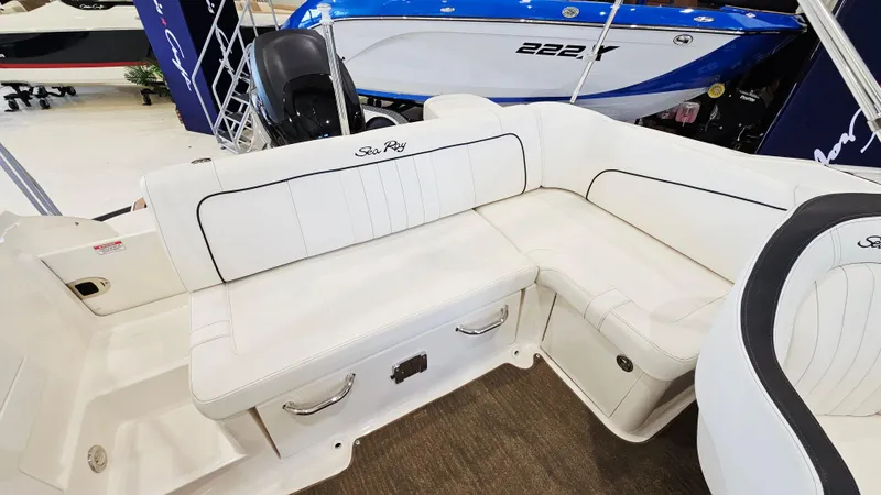 Slide: The Image of 2014 Sea Ray 220 Sundeck Outboard with white cushioned seating in a showroom. - 7