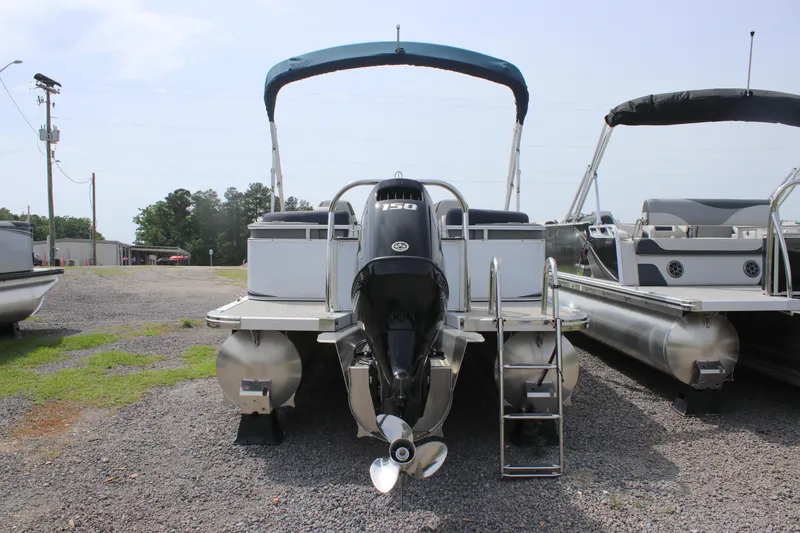 Slide: The Image of 2024 Avalon LSZ Quad Lounger pontoon boat with outboard motor and ladder, parked on gravel. - 6