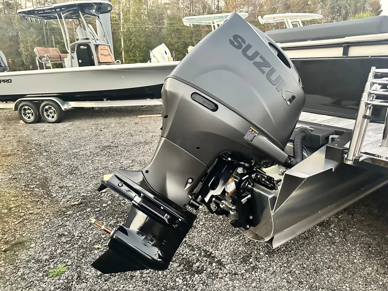 Slide: The Image of 2025 Avalon LSZ Versatile Rear Lounger with Suzuki outboard motor, parked on gravel. - 12