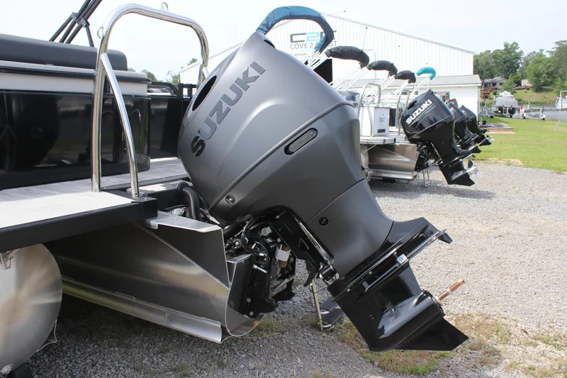 Slide: The Image of 2025 Avalon LSZ Versatile Rear Lounger with Suzuki outboard motor, parked on gravel. - 9