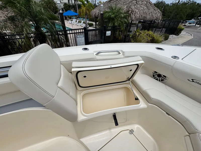 Slide: The Image of 2025 Scout 305 LXF boat interior with open storage compartment, white seating, and poolside view. - 17