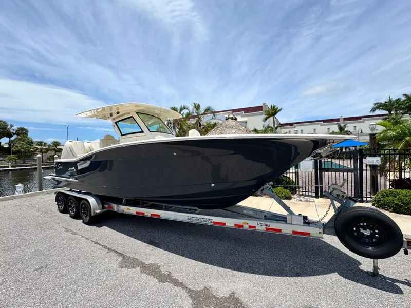Slide: The Image of 2025 Scout 305 LXF boat on trailer, parked near marina under clear sky. - 2