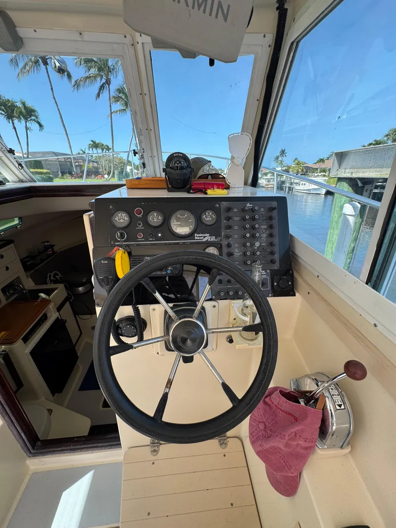 Slide: The Image of 1996 Albin Tournament Express helm with steering wheel, controls, and gauges, docked by palm trees. - 12