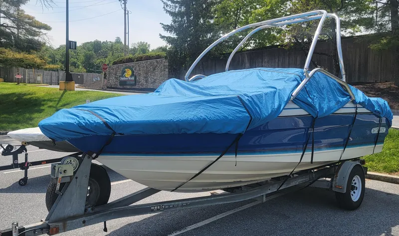 Slide: The Image of 1988 Bayliner 2150 Capri boat on trailer, covered with blue tarp, parked outdoors. - 5