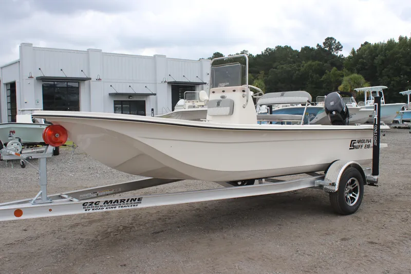 Slide: The Image of 2025 Carolina Skiff E18 JVX CC boat on trailer, parked outdoors near a building. - 0