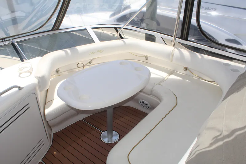 Slide: The Image of 2000 Sea Ray 480 Sedan Bridge interior with white seating and table on wooden deck. - 10