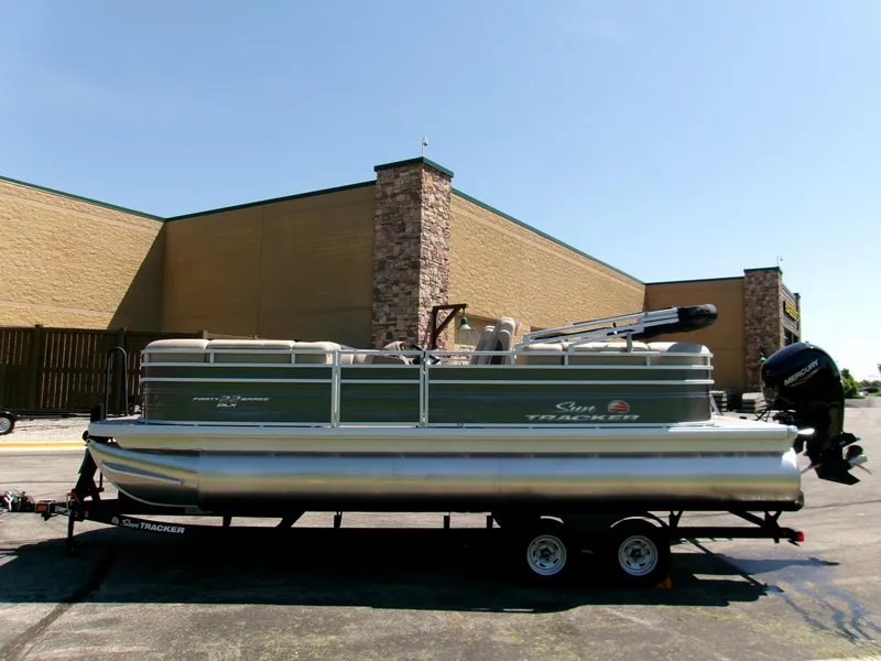 Slide: The Image of 2025 Sun Tracker Party Barge 22 DLX pontoon boat on trailer, parked outdoors. - 2